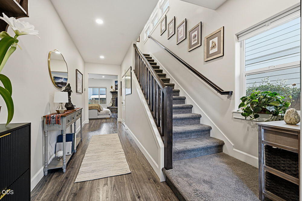 Entry hall with carpeted staircase, dark wood floors, and a view into a bedroom.
