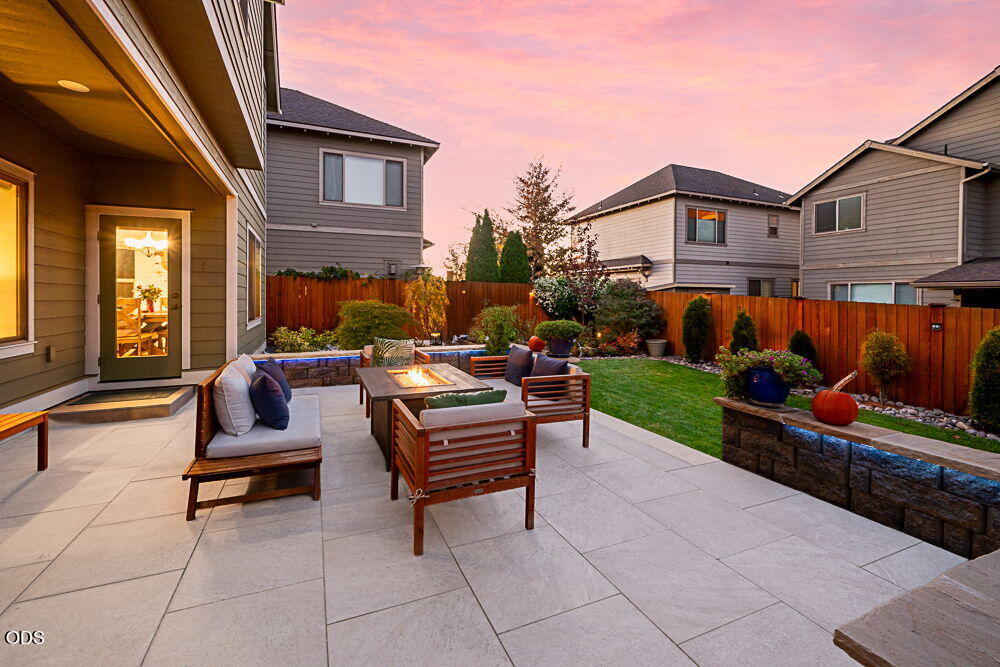 Backyard patio with outdoor seating, a lawn, and landscaped garden at dusk.