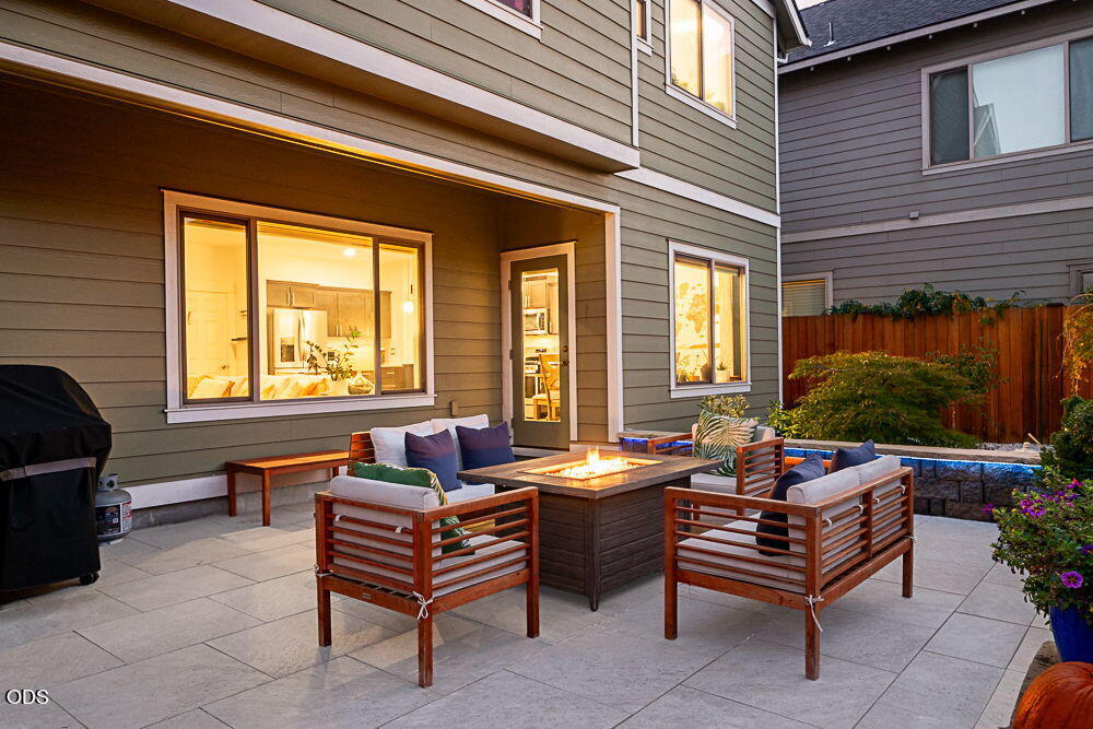 Furnished patio with lounge seating around a glowing fire table beside the home.