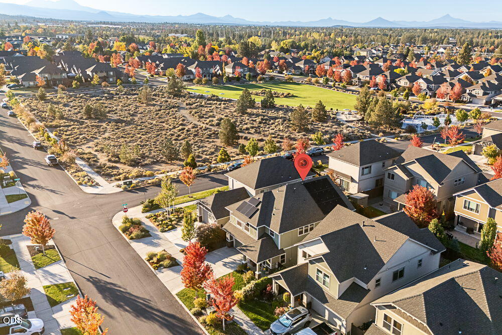 Aerial view of a residential neighborhood beside open scrubland, with autumn trees and distant mountains.