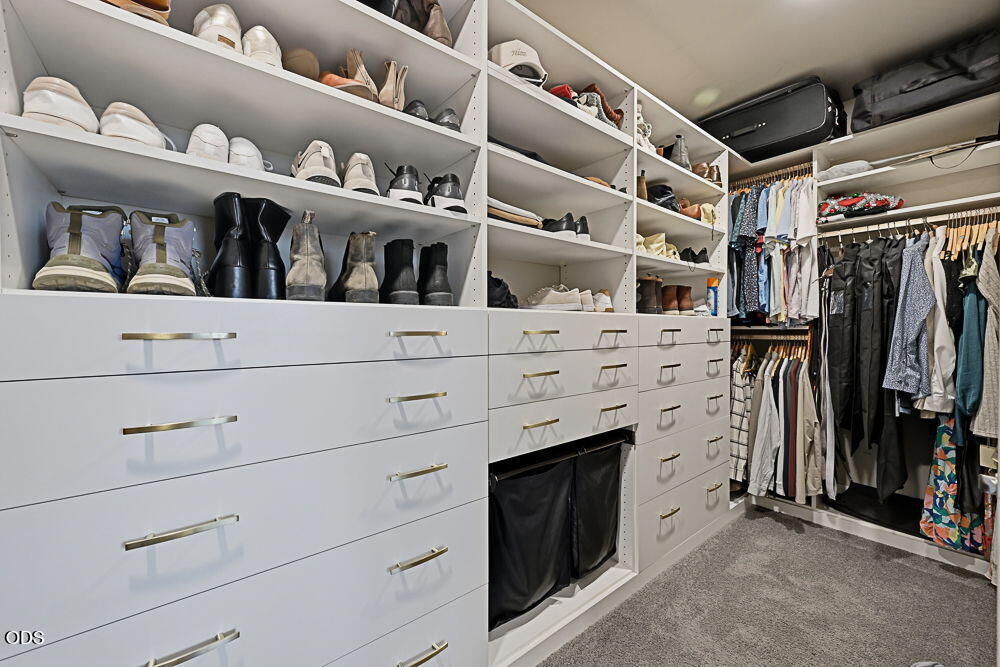Walk-in closet with built-in drawers, shoe shelves, hanging clothes, and gray carpet.