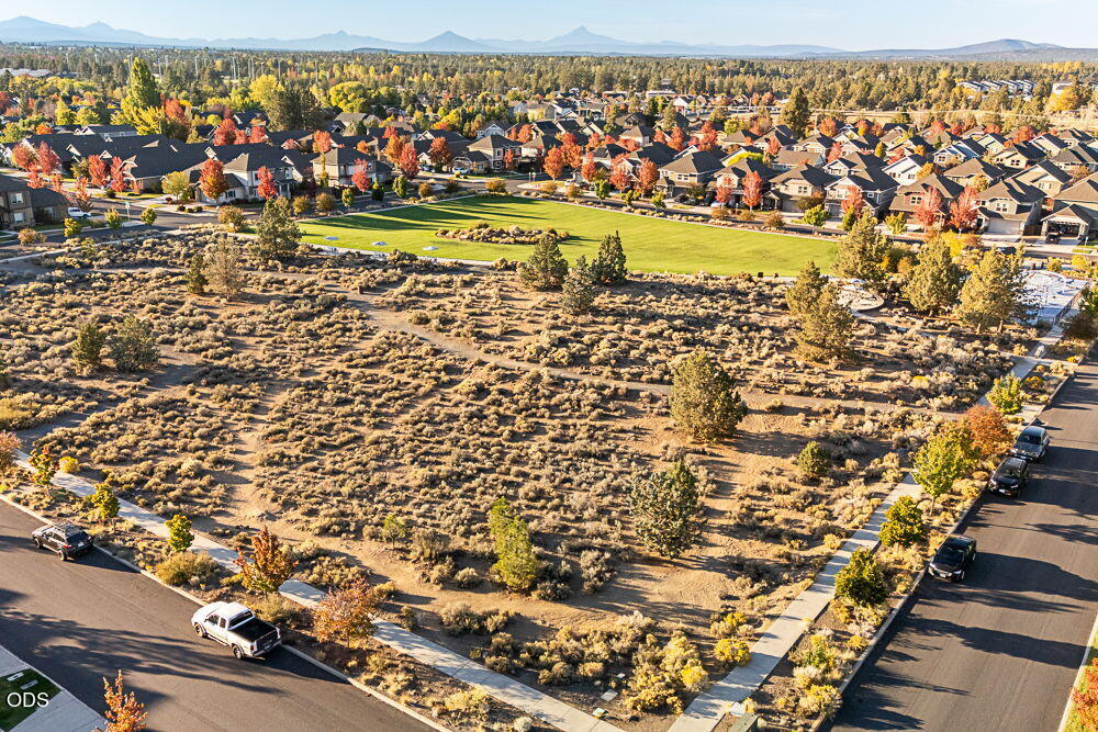 Aerial view of Bend homes beyond open scrubland, with autumn trees and mountains on the horizon.