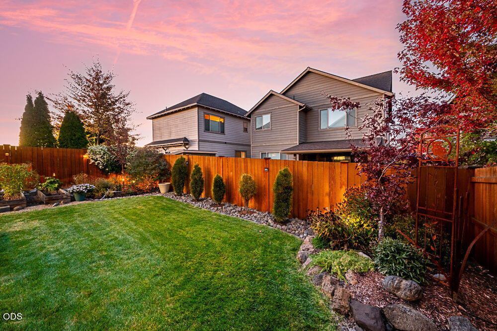 House viewed from a landscaped backyard with a wooden fence and red autumn foliage.