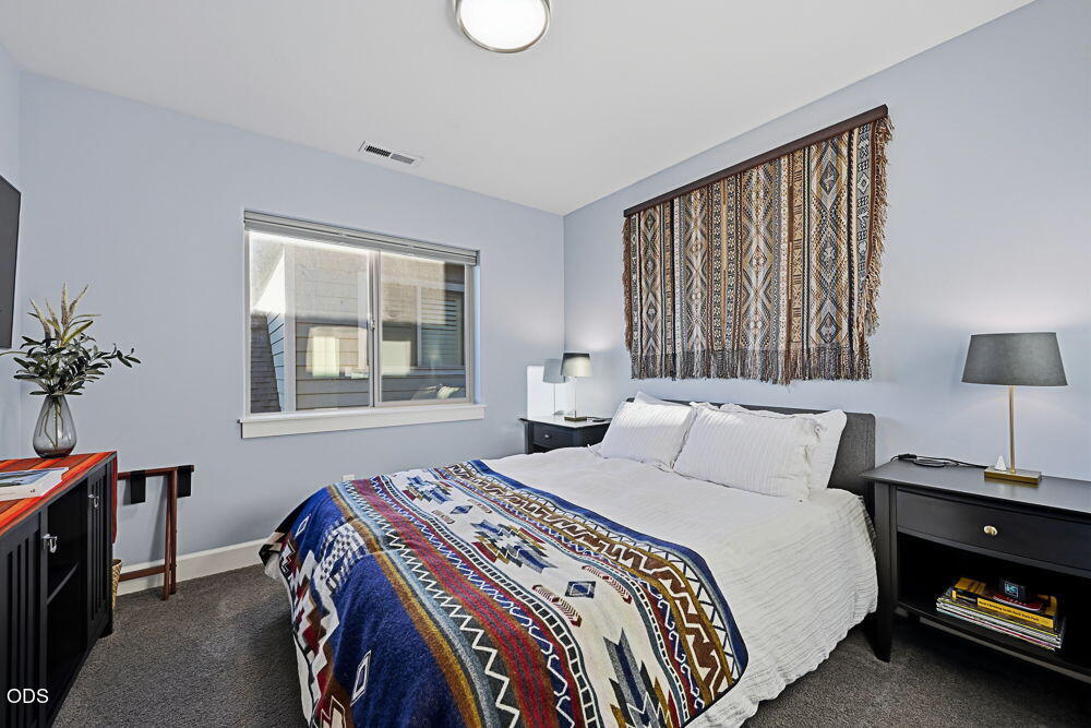 Bedroom with a large bed, colorful patterned blanket, woven wall hanging, and window.