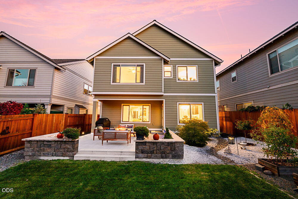 Rear of a two-story gray home with a raised stone patio and outdoor seating at dusk.
