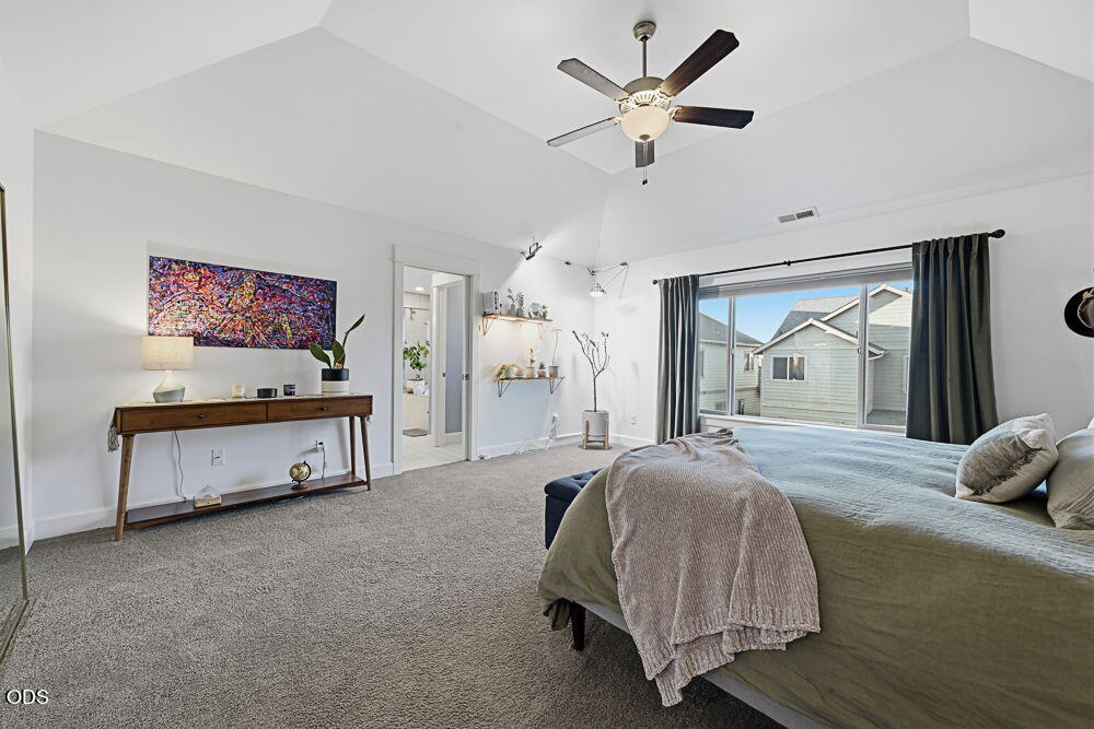 Furnished bedroom with a vaulted ceiling, ceiling fan, and large curtained window.