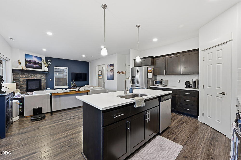 Open-plan kitchen with a large island, dark cabinetry, stainless steel appliances, and a stone fireplace.