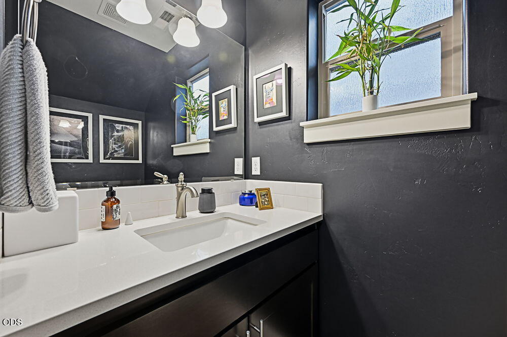 Bathroom vanity with a white sink, dark walls, and a window with a potted plant.