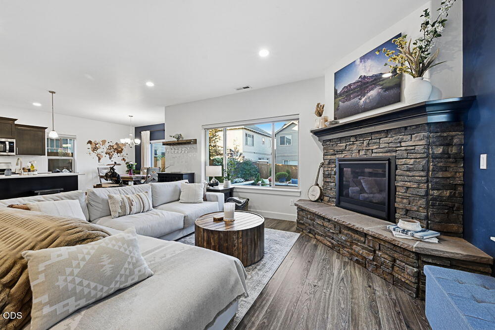 Living room with a white sectional, stone fireplace, and wide window overlooking neighboring homes.