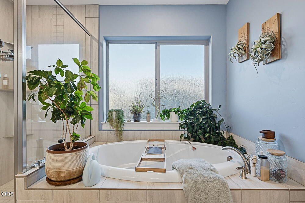 Bathroom with a corner soaking tub, frosted window, potted plants, and wooden bath tray.