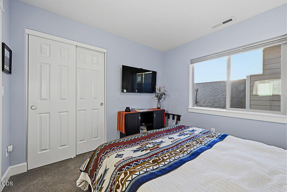 Bedroom with a patterned blue-and-white bedspread, sliding closet doors, and a wall-mounted television.