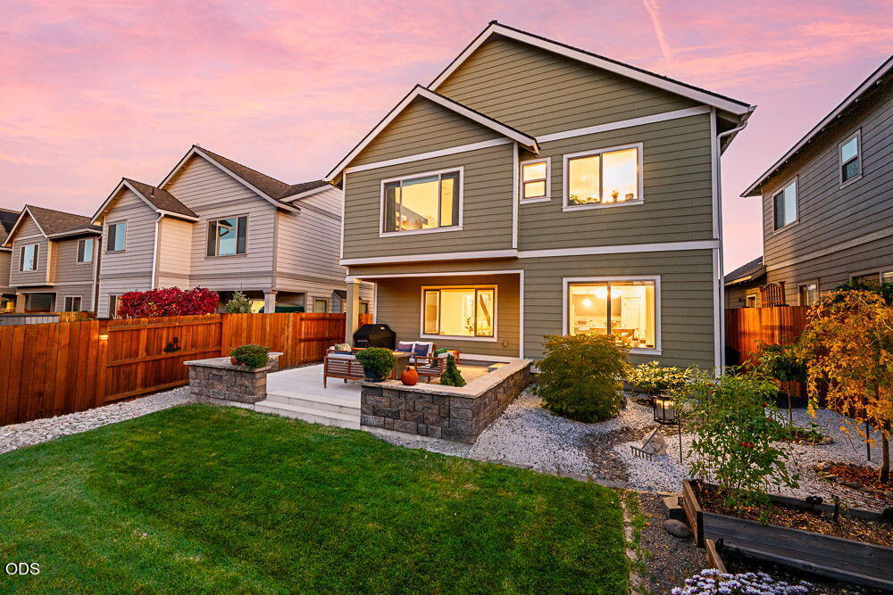 Two-story gray home with a stone patio and fenced yard at sunset.