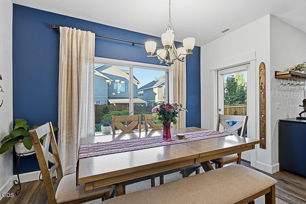 Dining room with a wooden table, chandelier, and blue accent wall beside large windows.