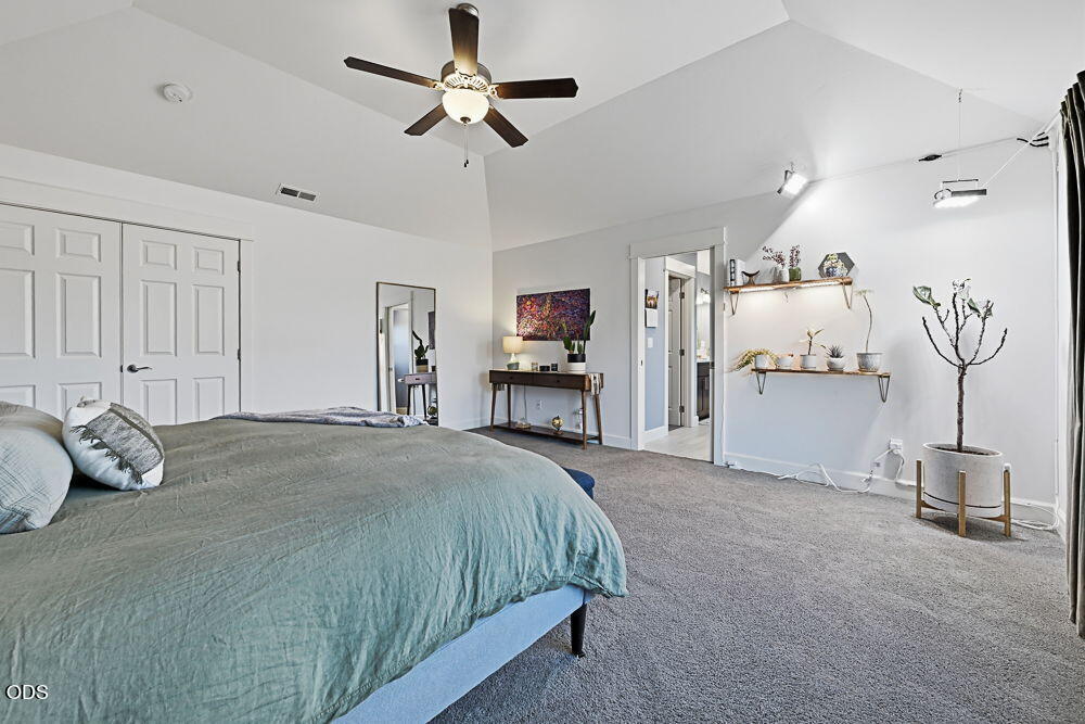 Staged bedroom with a large bed, vaulted ceiling, ceiling fan, and carpeted floor.