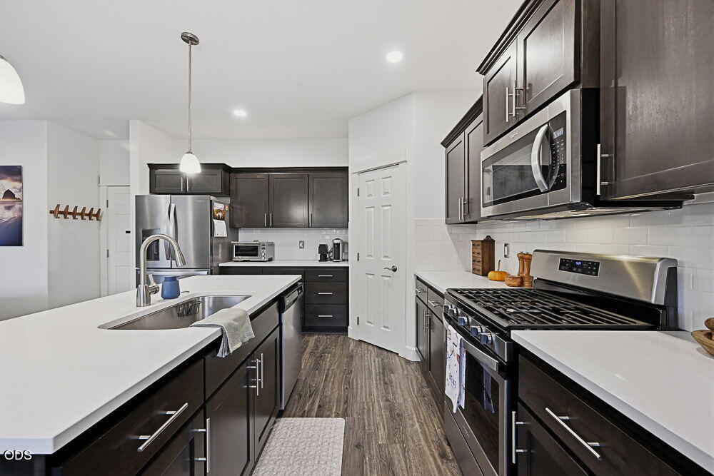 Kitchen with dark cabinets, white countertops, a sink island, and stainless steel appliances.