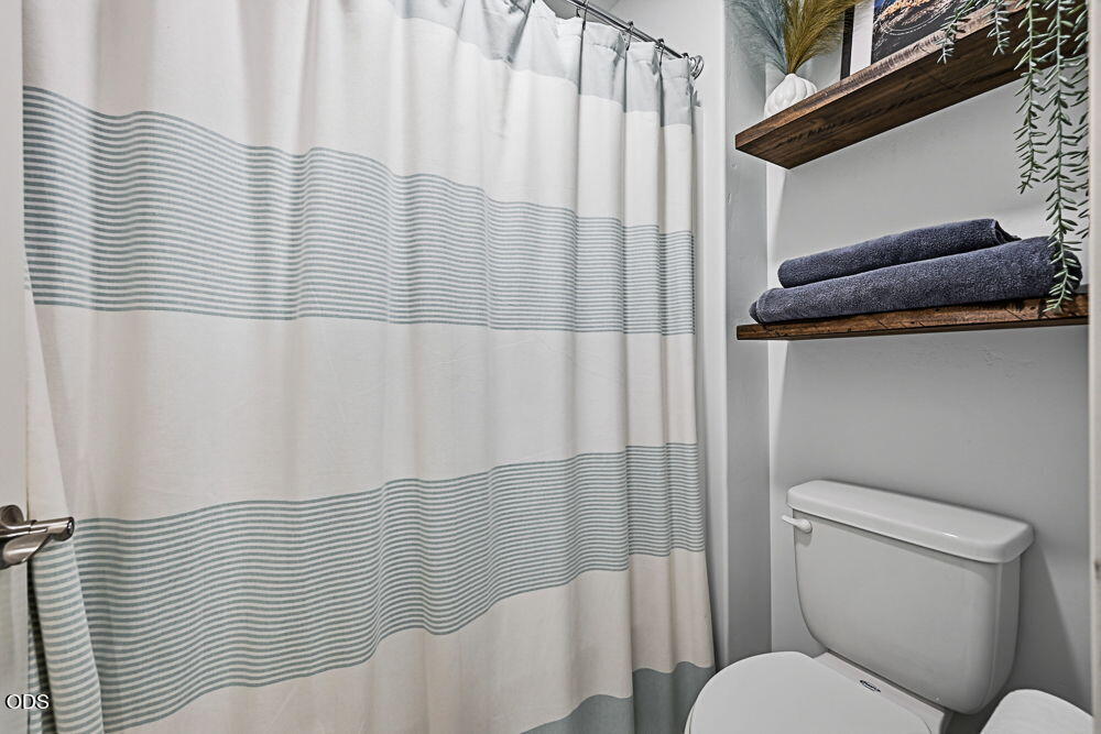 Bathroom with a striped shower curtain and wall shelves holding folded towels.