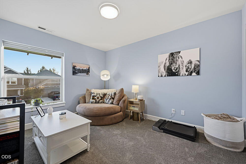 Sitting room with pale blue walls, a rounded tan chair, and a large window overlooking neighboring homes.