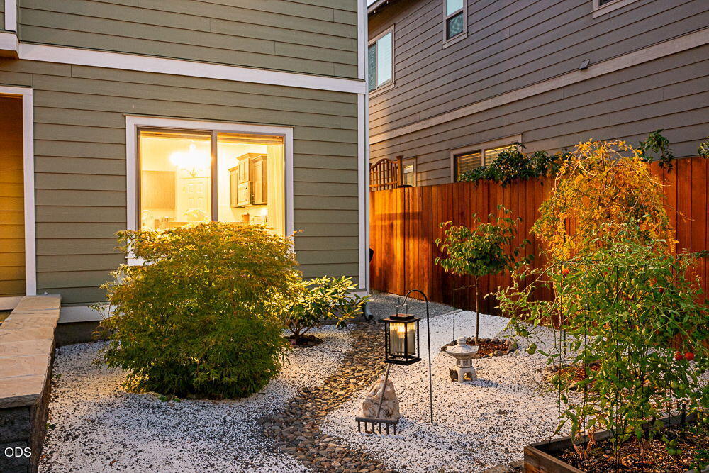 Home courtyard with white gravel, a winding stone path, shrubs, and a wooden privacy fence.
