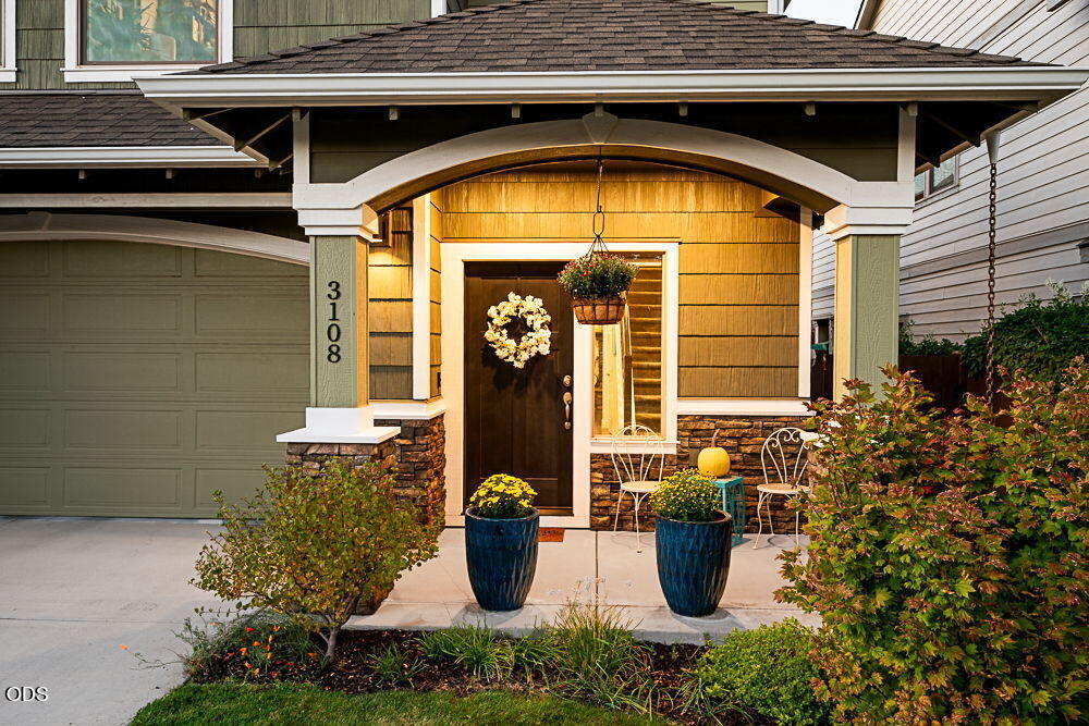 Home entrance with an arched porch, green garage, stone accents, and potted flowers.