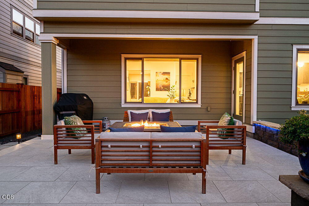 Covered patio with lounge seating around a fire pit, warmly lit at dusk.