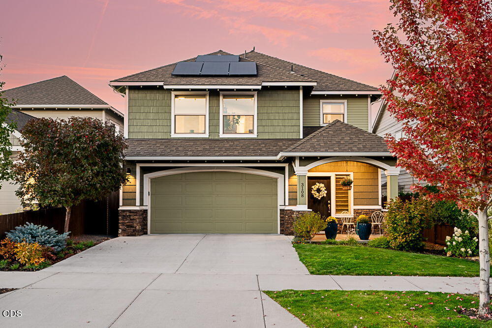 Two-story green home with rooftop solar panels and a landscaped front yard at dusk.