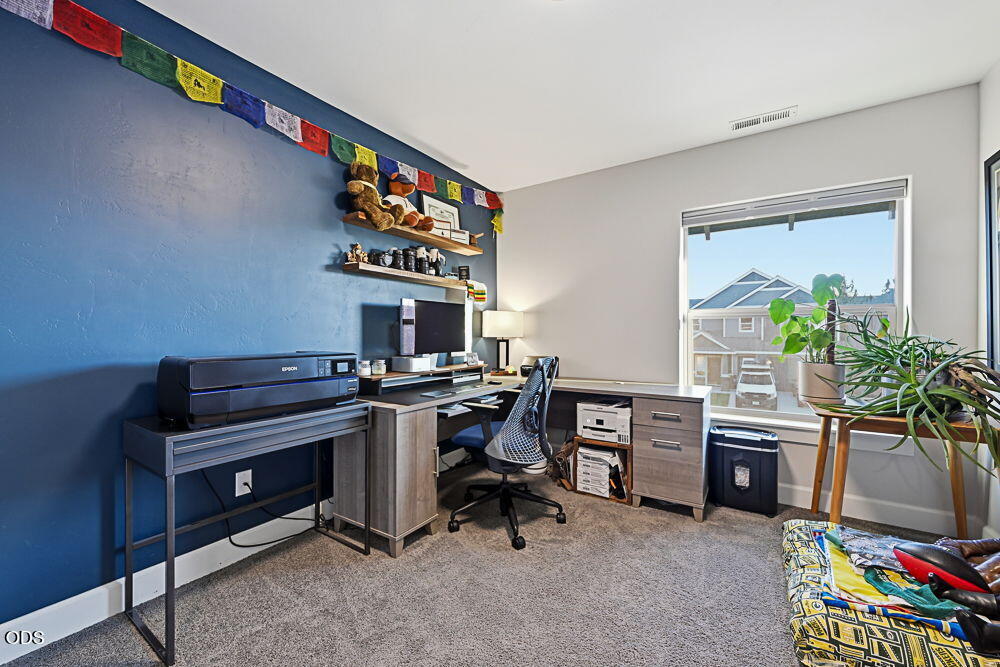 Furnished home office with a blue accent wall, L-shaped desk, and large window.