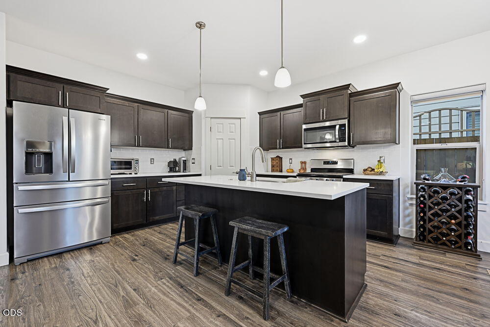 Kitchen with dark cabinets, stainless steel appliances, and a large white island with two stools.