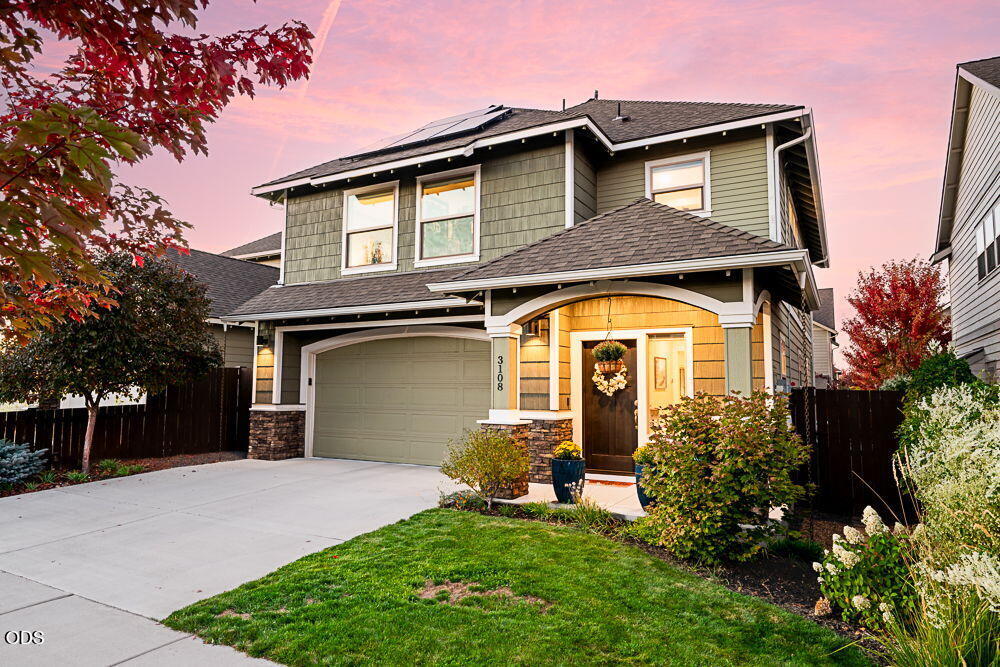 Two-story gray-green home with solar panels, double garage, and covered entry at dusk.