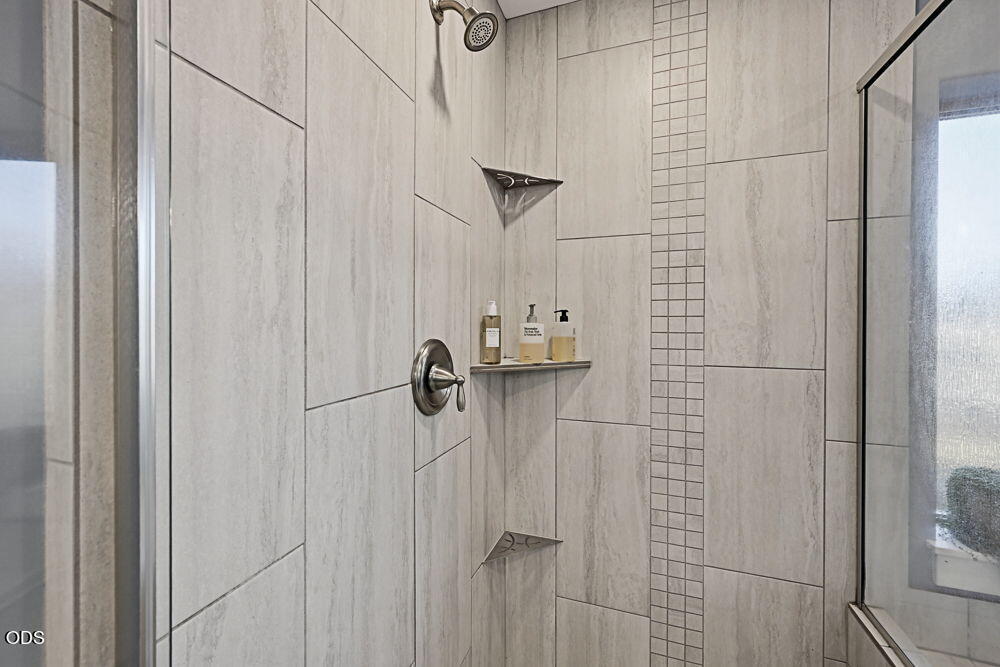 Tiled shower with glass enclosure, vertical mosaic accent strip, and built-in corner shelves.