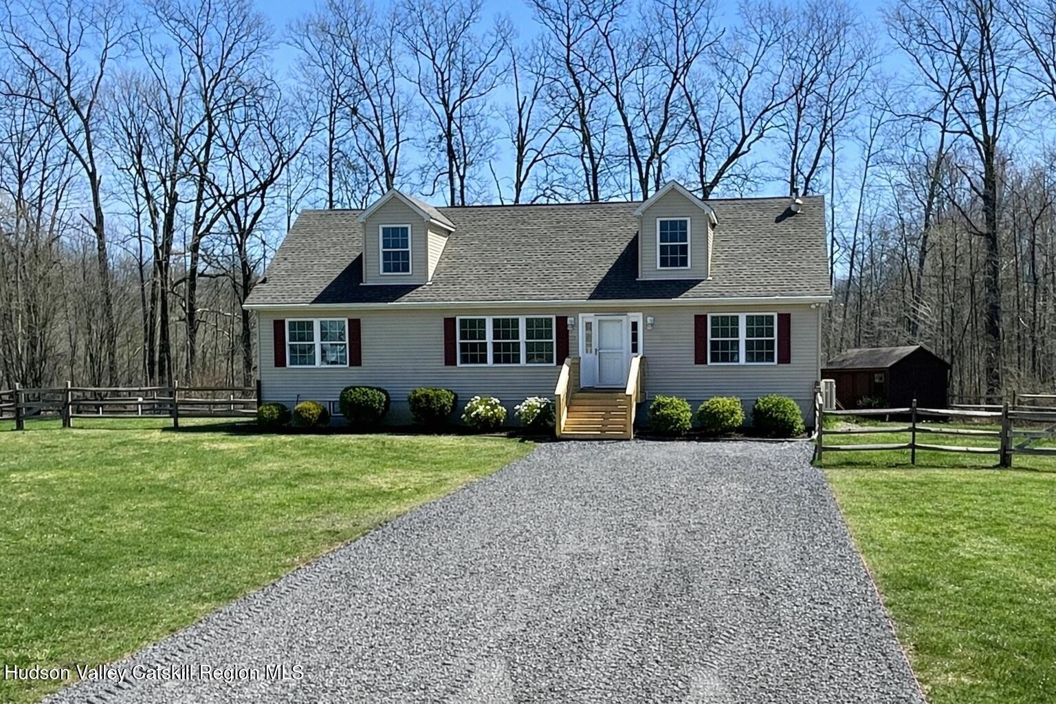 Gray house with dormer windows and red shutters at the end of a gravel driveway.