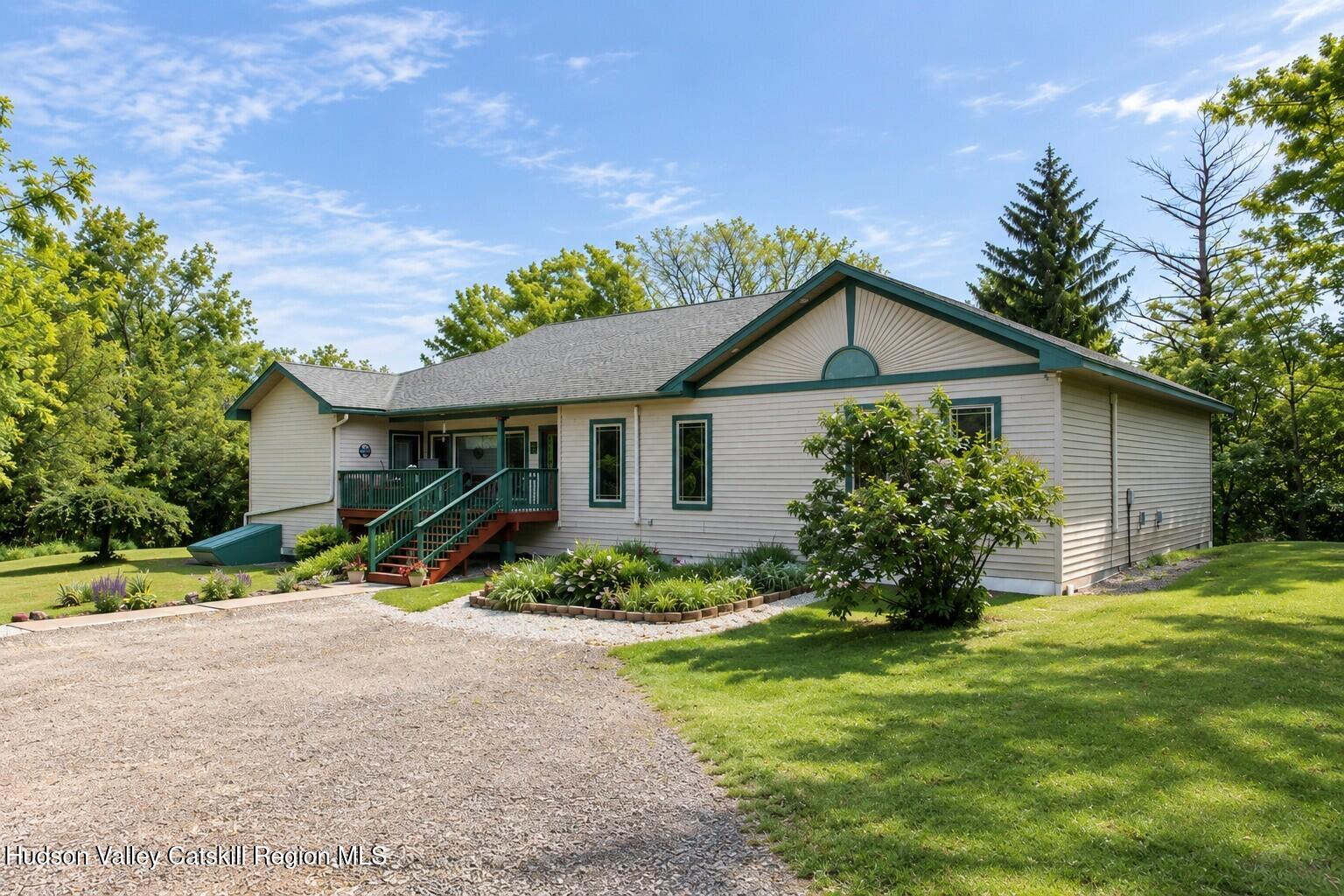 Single-story home with green-trimmed gables, a raised deck, landscaped garden, and gravel driveway.