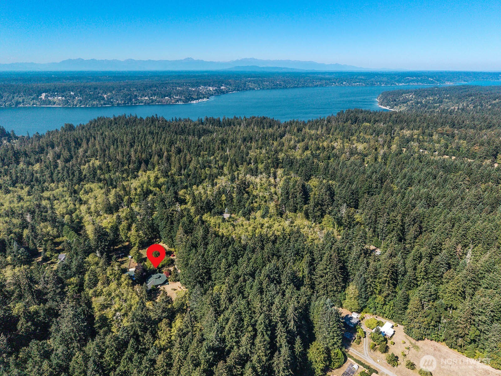 Aerial view of a forested property with water and distant mountain views, marked by a red pin.