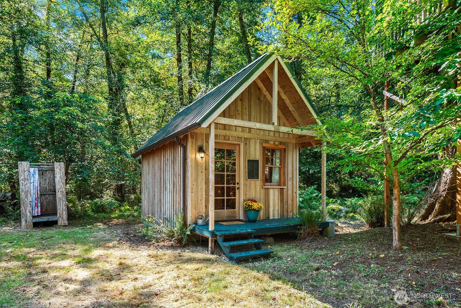 Small wood cabin with a steep green roof and porch nestled among trees.