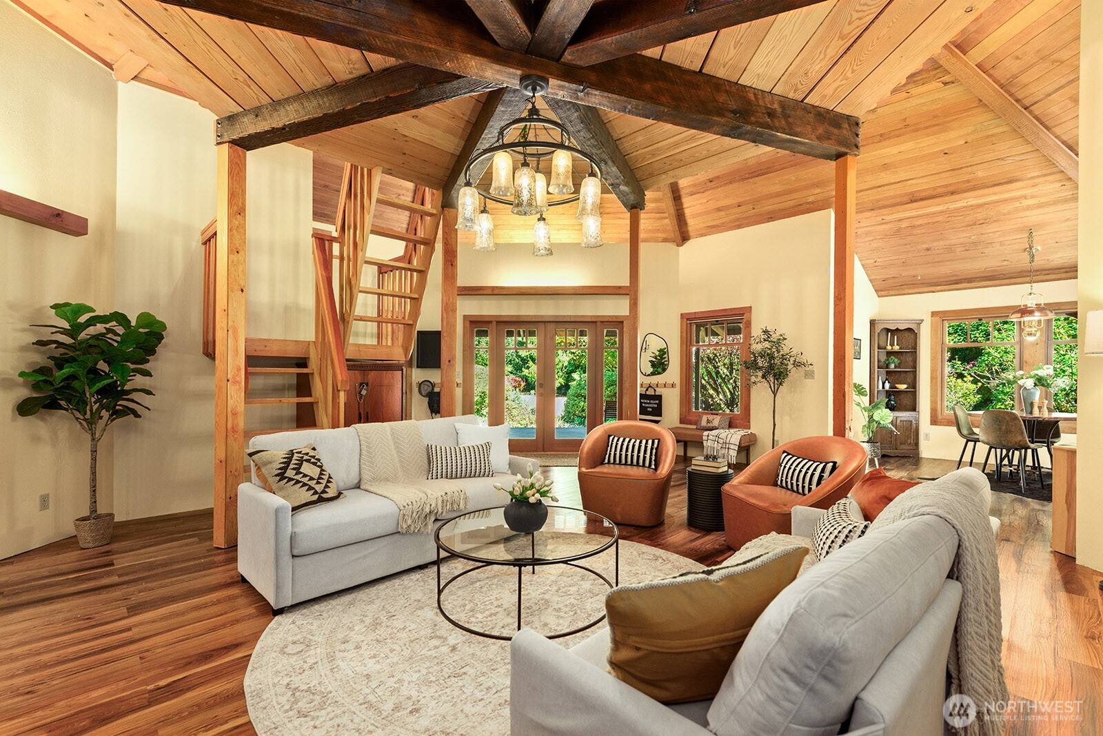 Living room with vaulted wood ceiling, exposed beams, chandelier, and an open dining area.