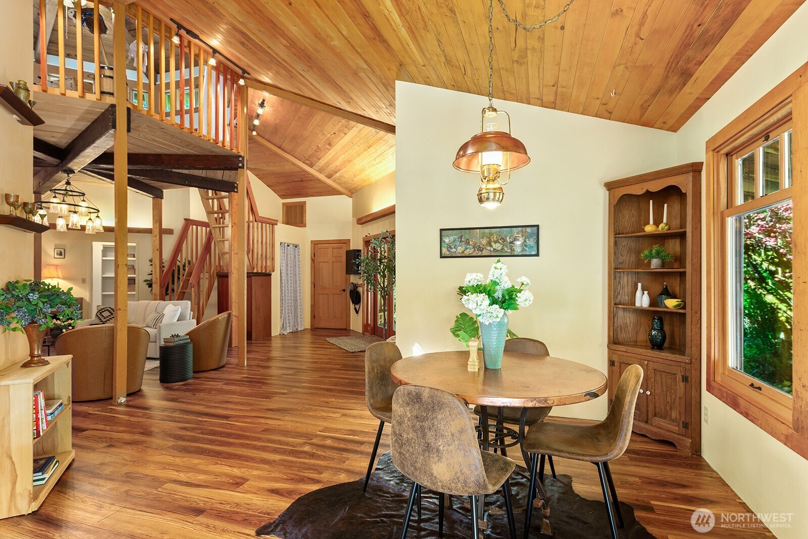 Open dining and living area with a vaulted wood ceiling, loft staircase, and round dining table.