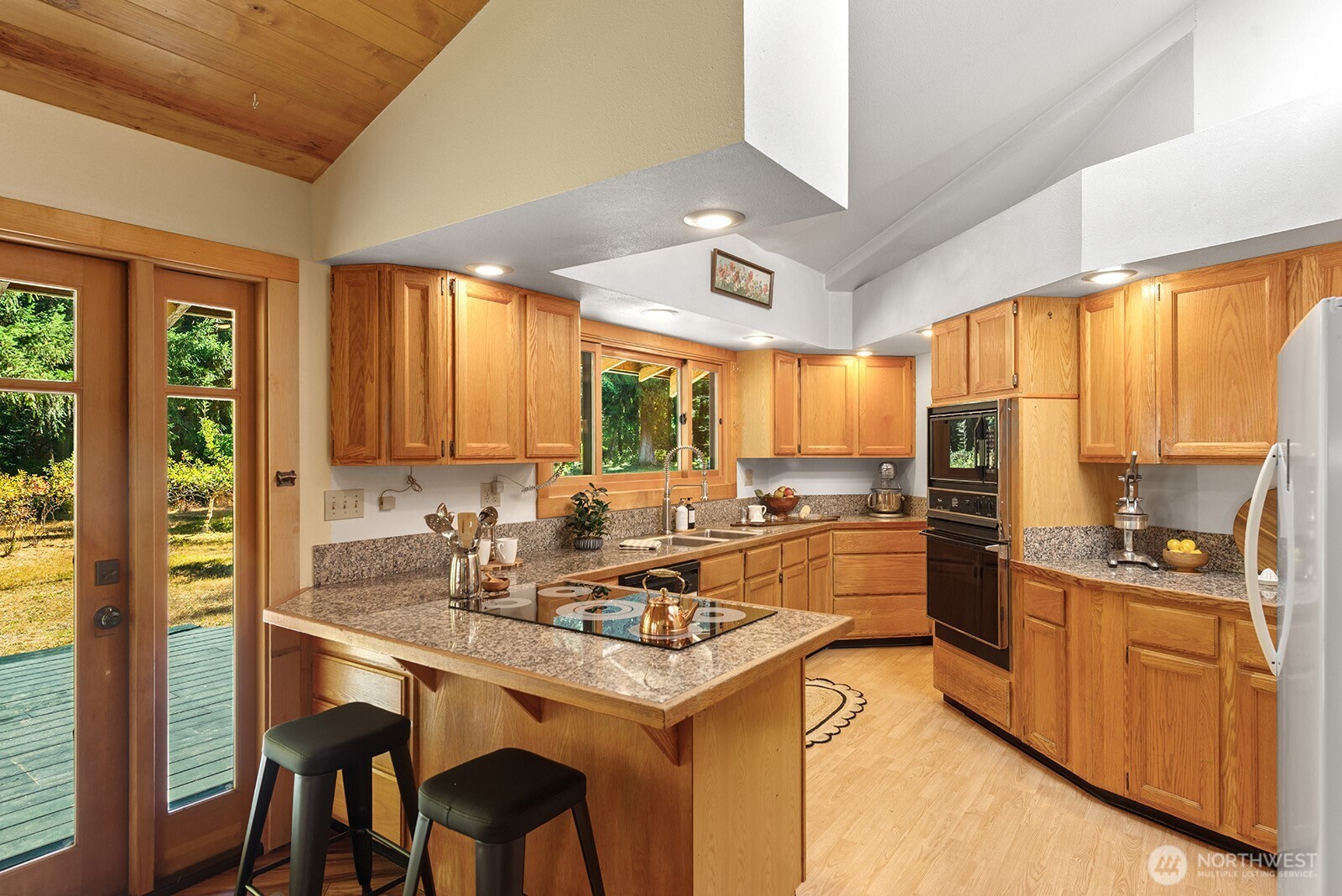 Kitchen with oak cabinets, granite counters, a cooktop island, and glass doors to a deck.