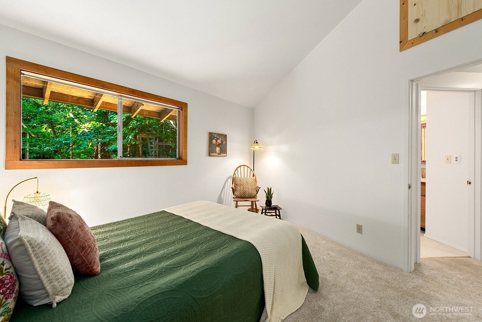 Bedroom with a green quilted bed and a wide wood-trimmed window overlooking trees.