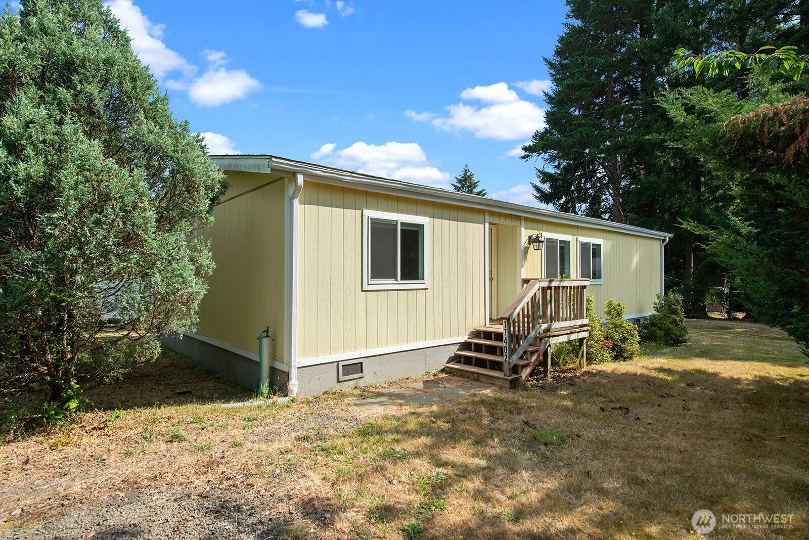 Pale yellow single-story home with a small wooden porch, steps, and a dry, tree-lined yard.