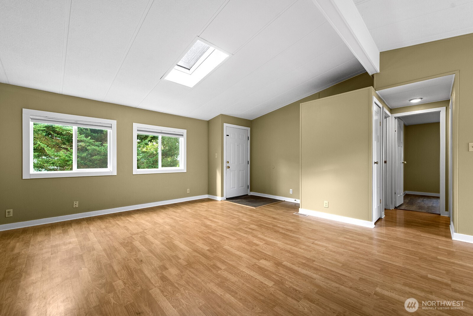 Empty room with wood-look flooring, two windows, a skylight, and several doorways.