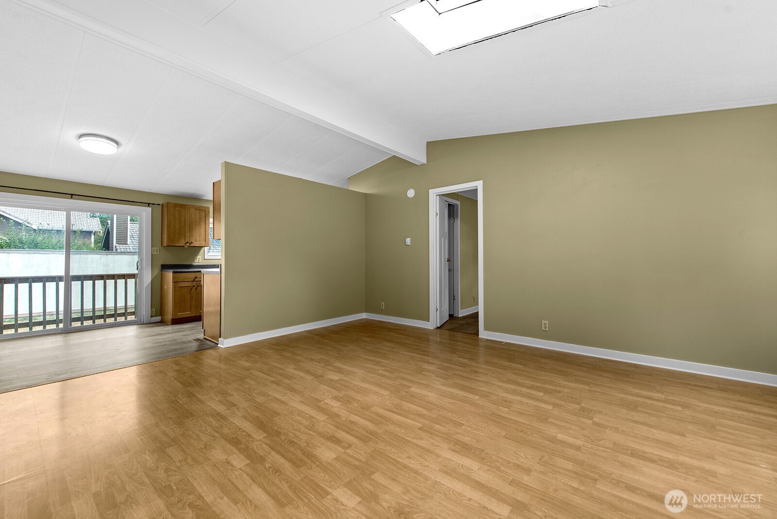 Vacant living room with wood-look floors, a skylight, and sliding glass doors beside the kitchen.
