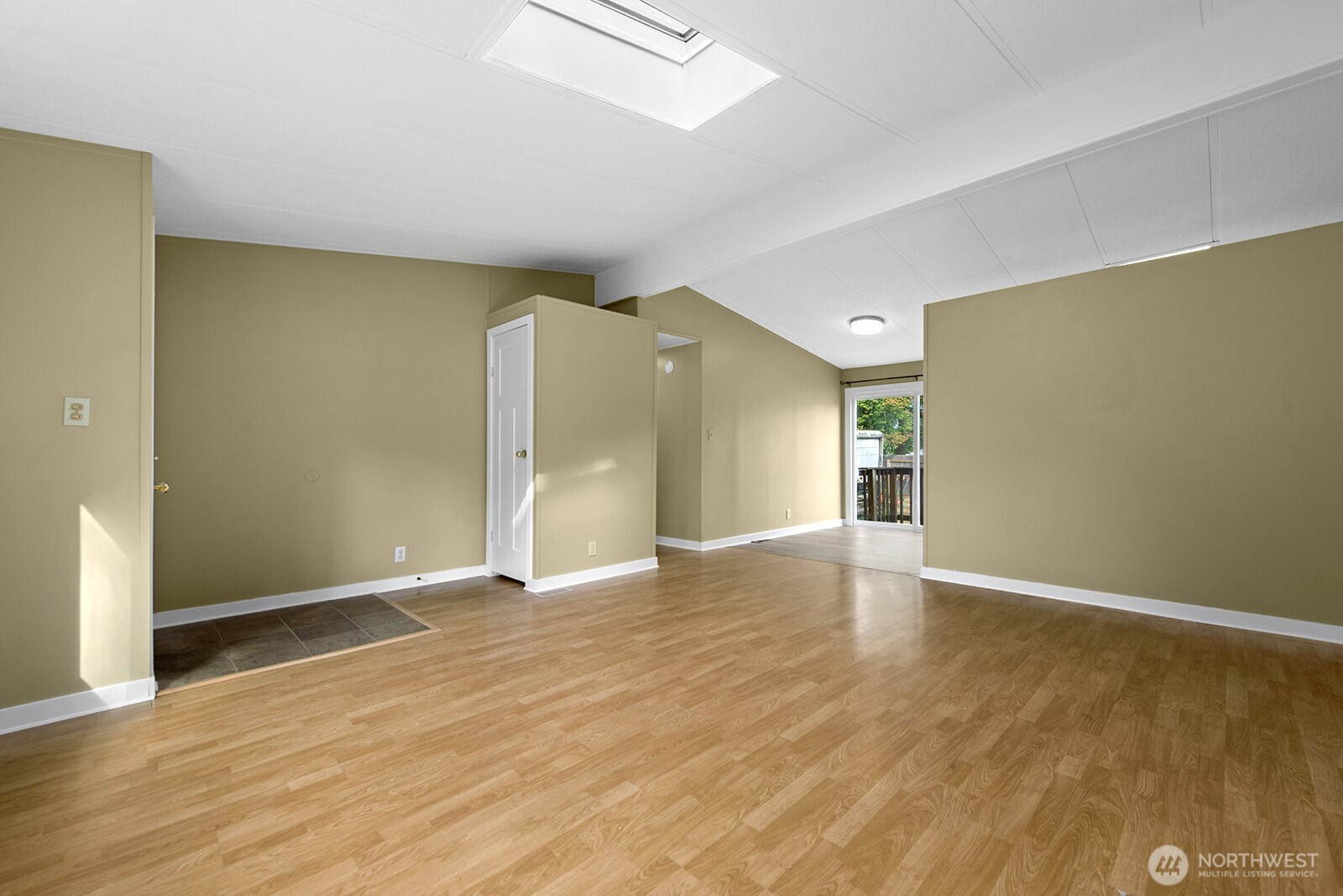 Empty living room with wood-look flooring, a skylight, and a sliding glass door to a deck.