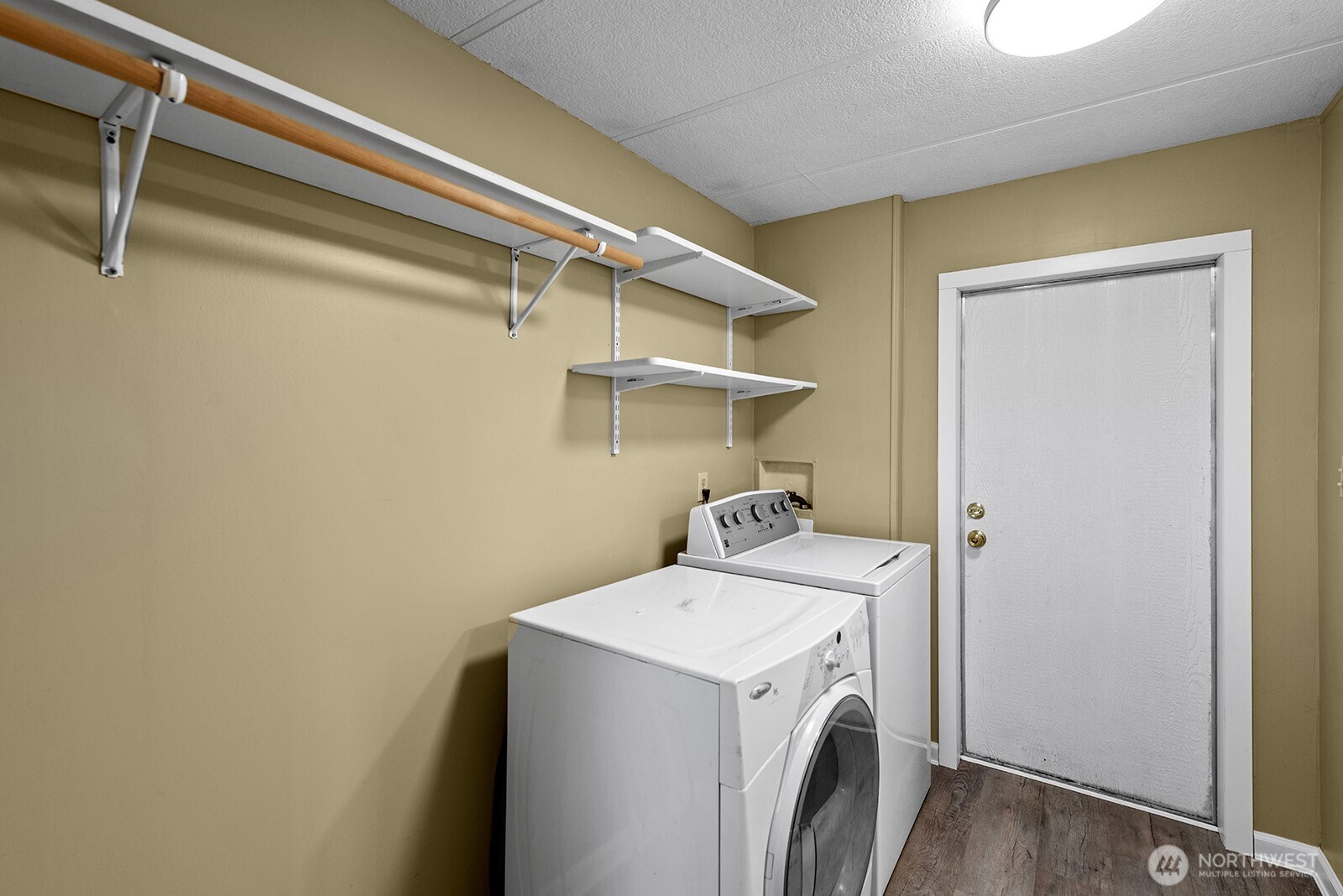 Laundry room with white washer and dryer beneath wall-mounted shelves and a hanging rod.