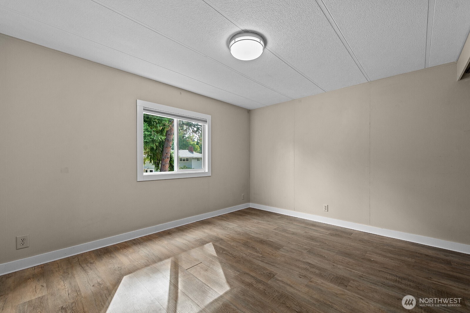 Empty room with wood-look flooring, beige walls, and a white-trimmed window.