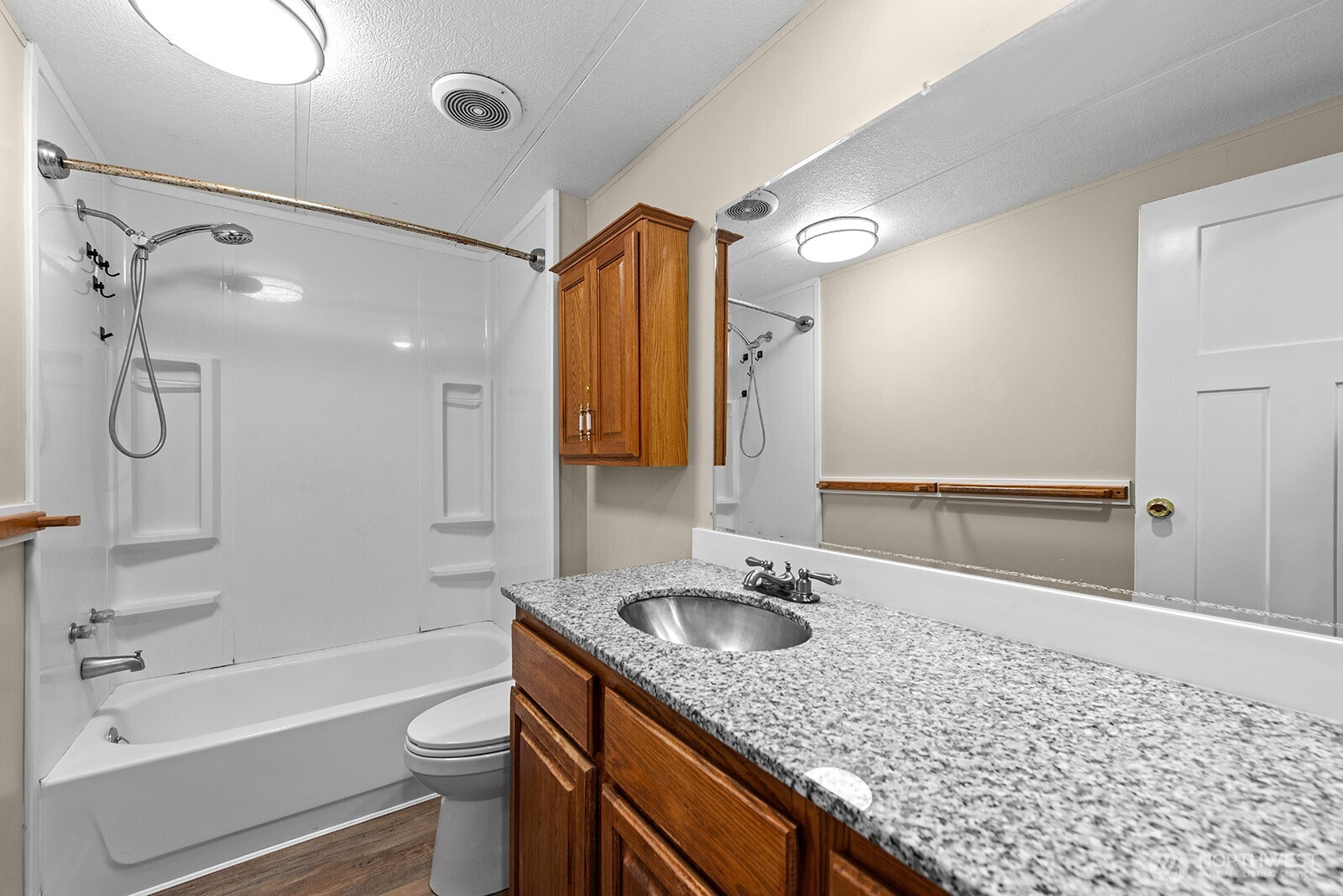 Bathroom with a tub-shower and wood vanity topped by a speckled granite counter.