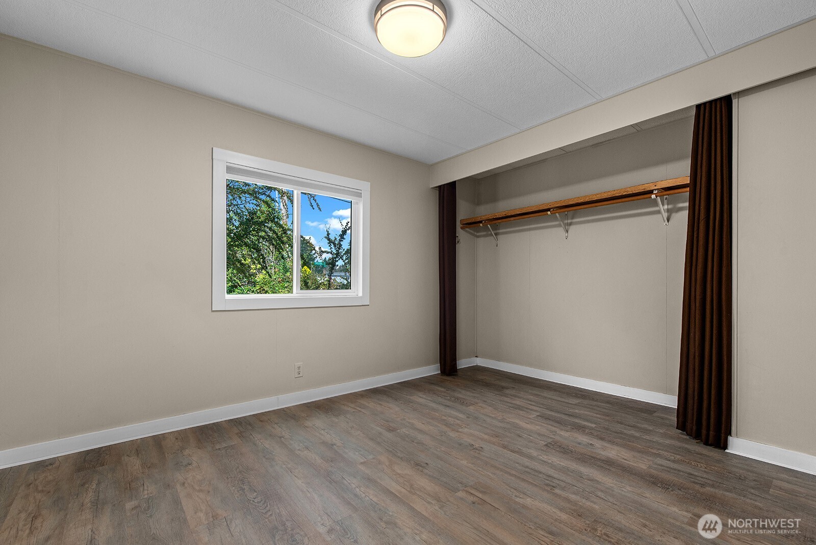 Empty bedroom with wood-look flooring, a window, and a curtained closet.