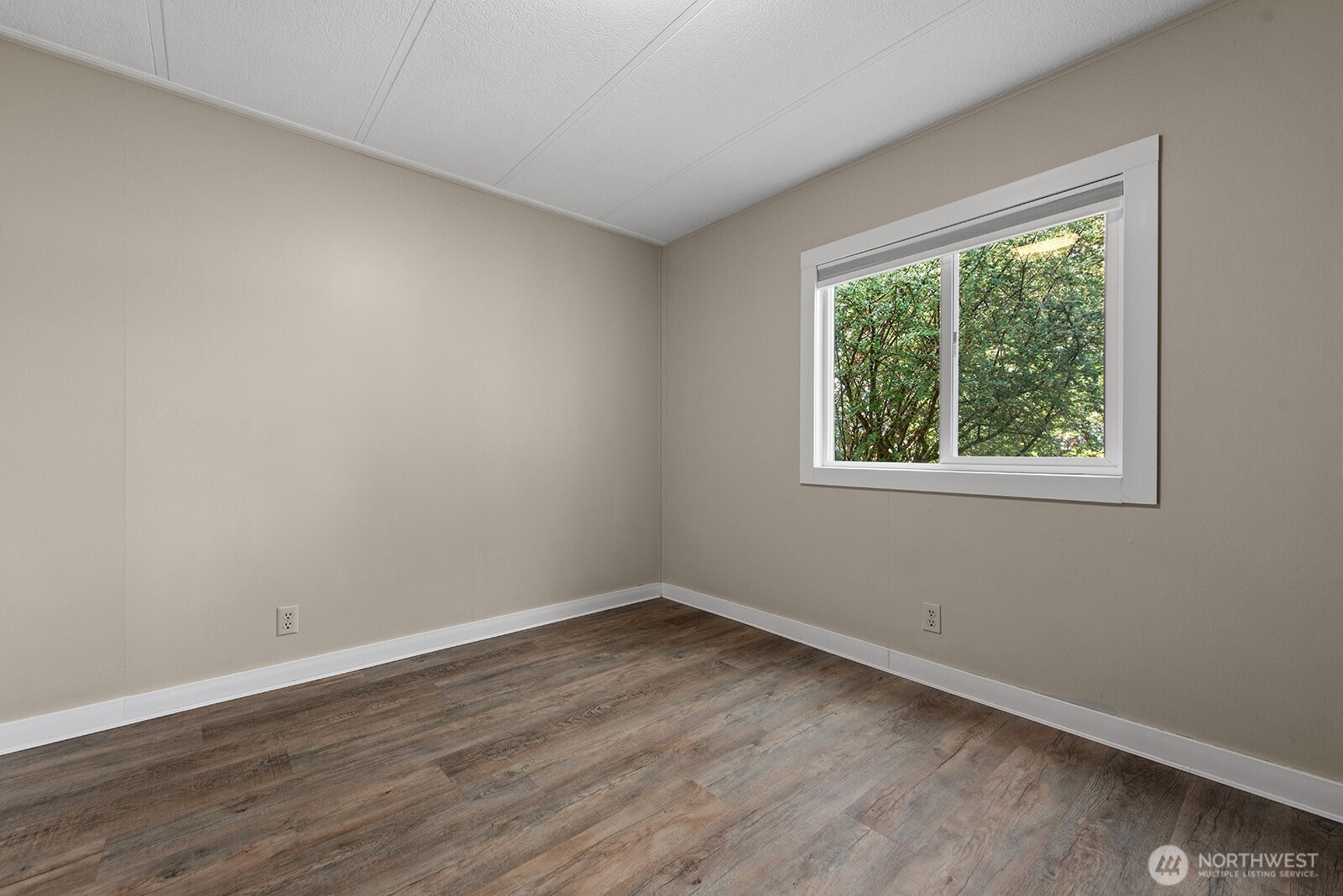 Empty room with wood-look flooring and a large window overlooking leafy trees.