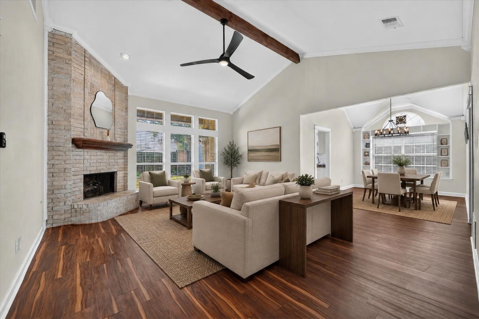 Staged living room with a brick fireplace, vaulted ceiling, and adjoining dining area.