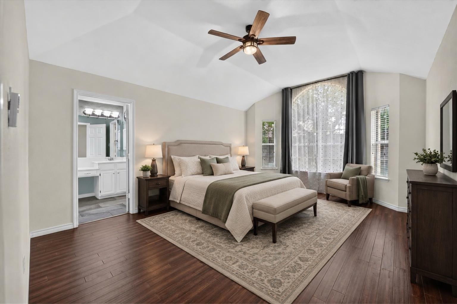 Primary bedroom with a vaulted ceiling, arched window, king-size bed, and adjoining bathroom.