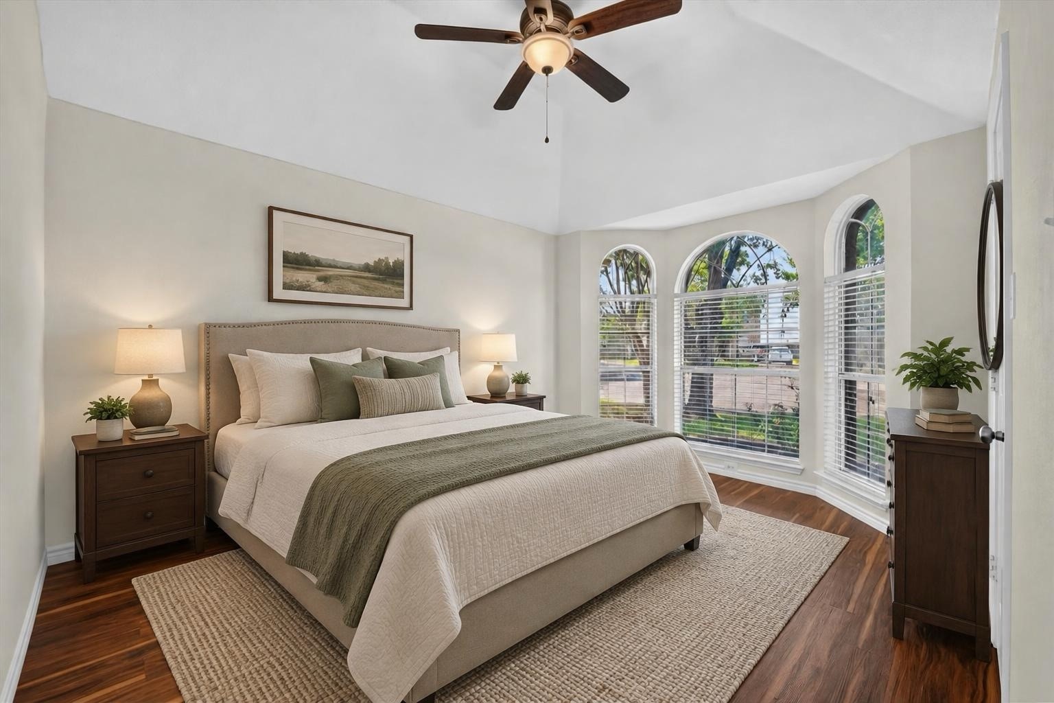 Staged bedroom with a large bed, vaulted ceiling, and three arched windows.
