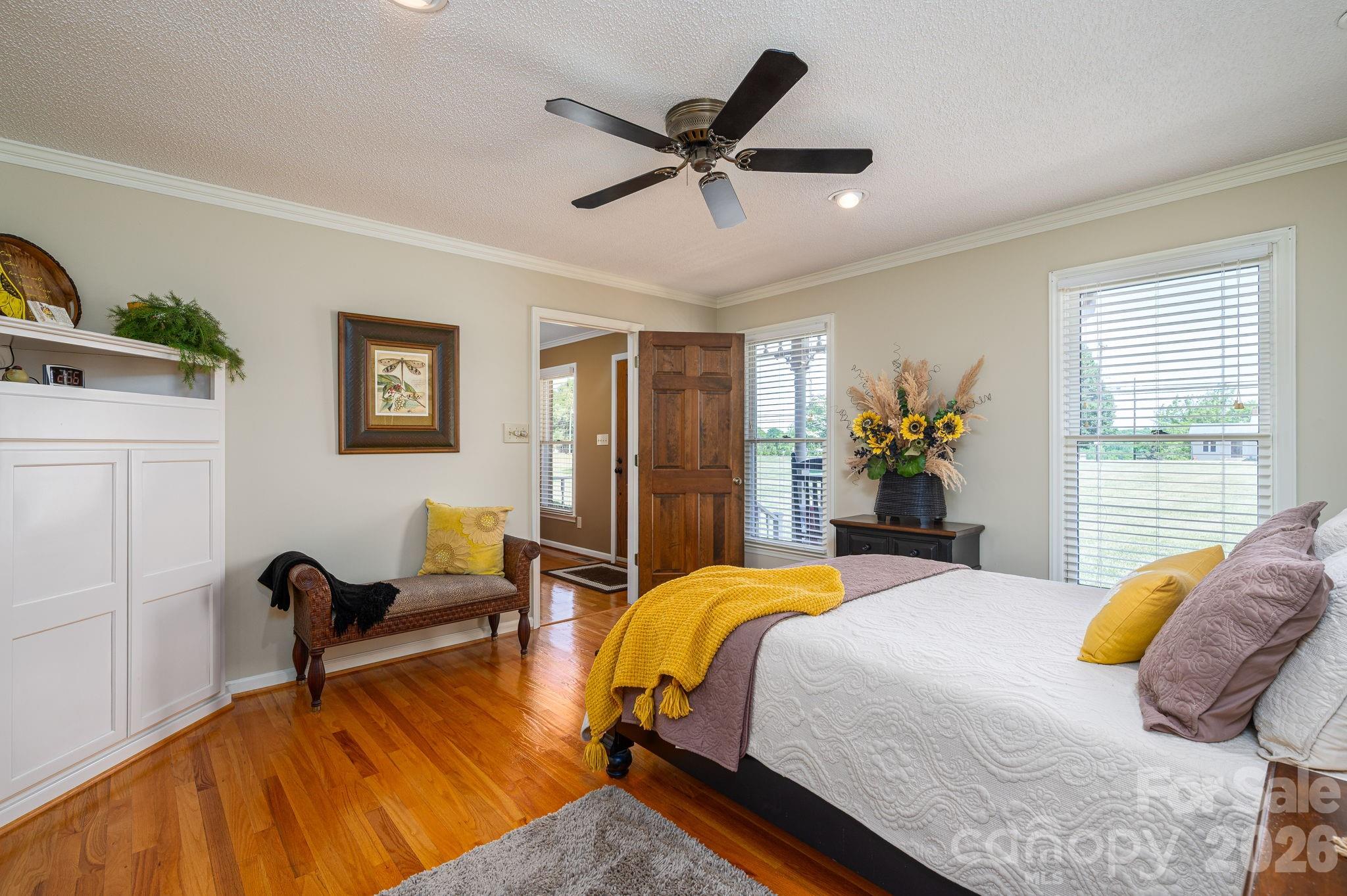 Bedroom with hardwood floors, a white built-in cabinet, and a bed accented with yellow and mauve bedding.
